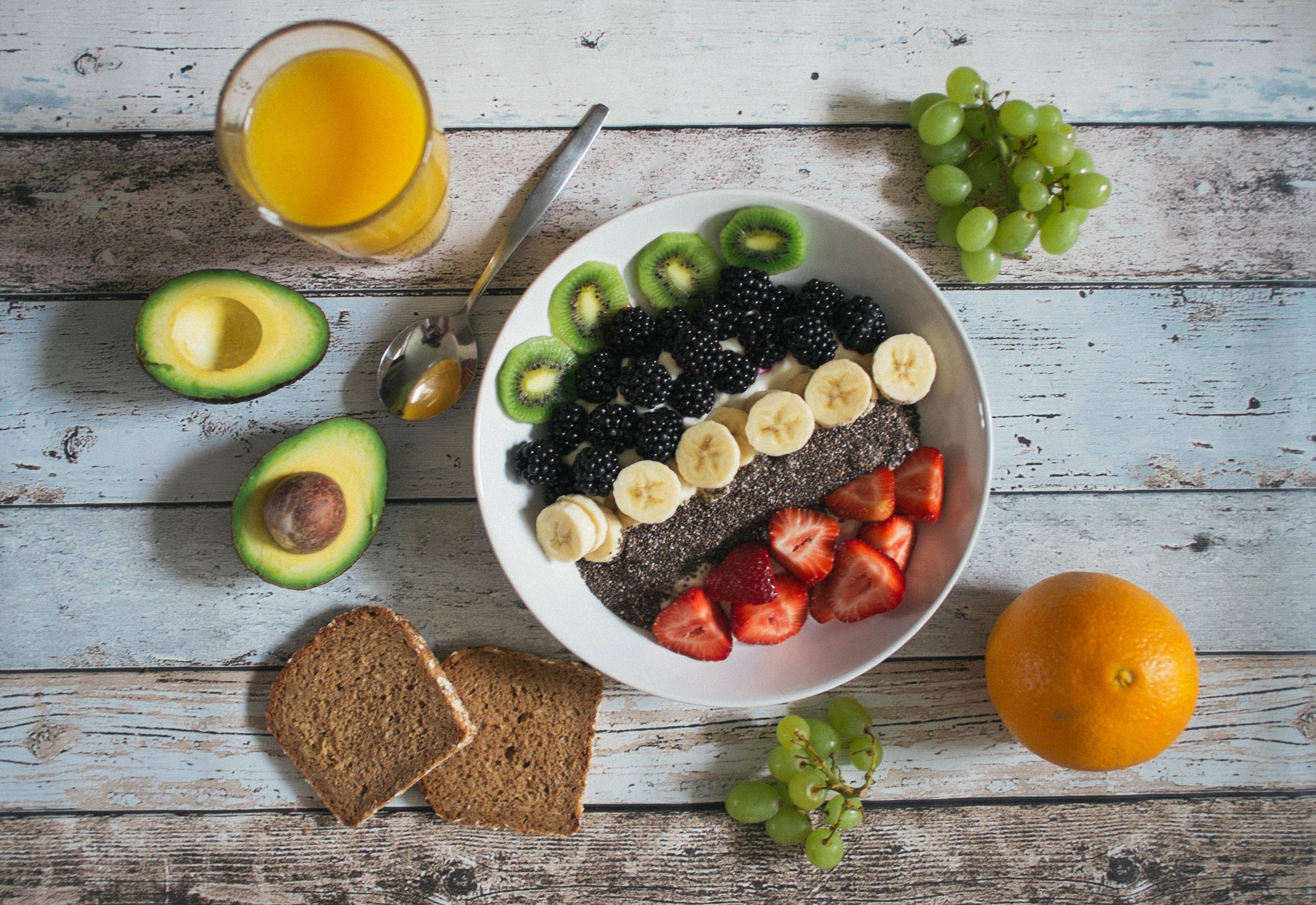 uma mesa com diversas frutas, no centro há um prato branco com frutas cortadas